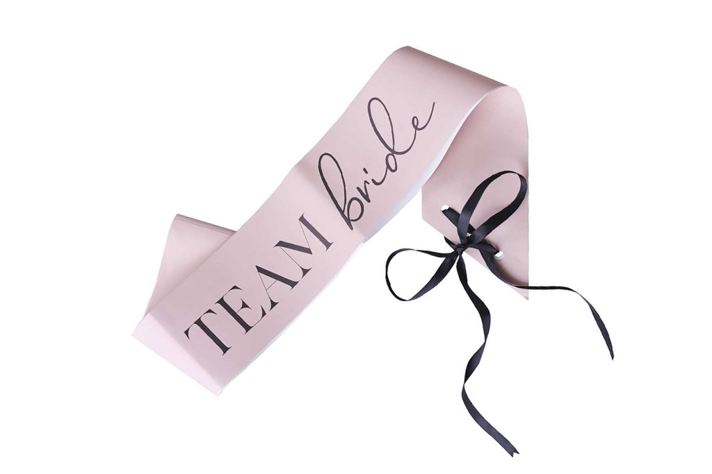 Lenta Team bride roze sa crnom mašnom Lenta Team bride roze sa crnom mašnom – pastel roze papirna lenta sa crnim TEAM bride natpisom i crnim satenskim trakama za vezivanje